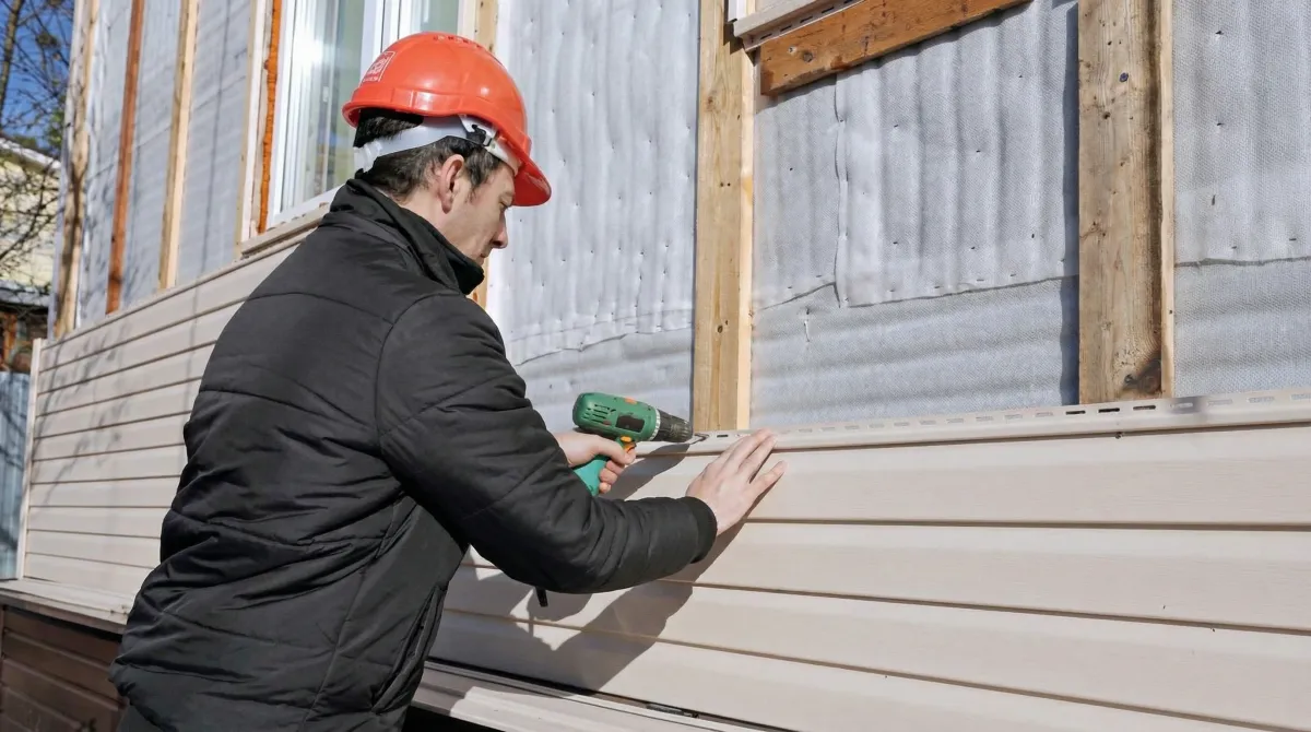 Siding replacement professional using a power drill to install new tan vinyl siding on a home exterior in Chula Vista, CA
